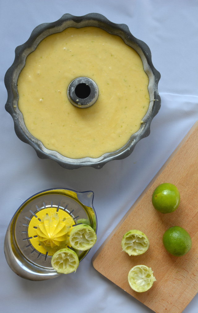 top view of a round cake tray with a central hole filled with lime and lychee batter mixture. A squeezed lime and a squeezer are placed beside the cake tray