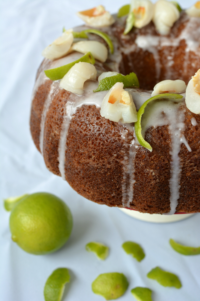 half side view of Lime and Lychee Cake with a drizzle of icing, garnished with lime zest and lychee, accompanied by a fresh lime on the side