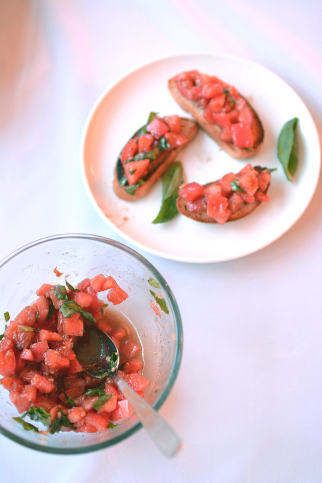 Homemade bruschetta served on a white place with a bowl of extra tomato and basil topping.