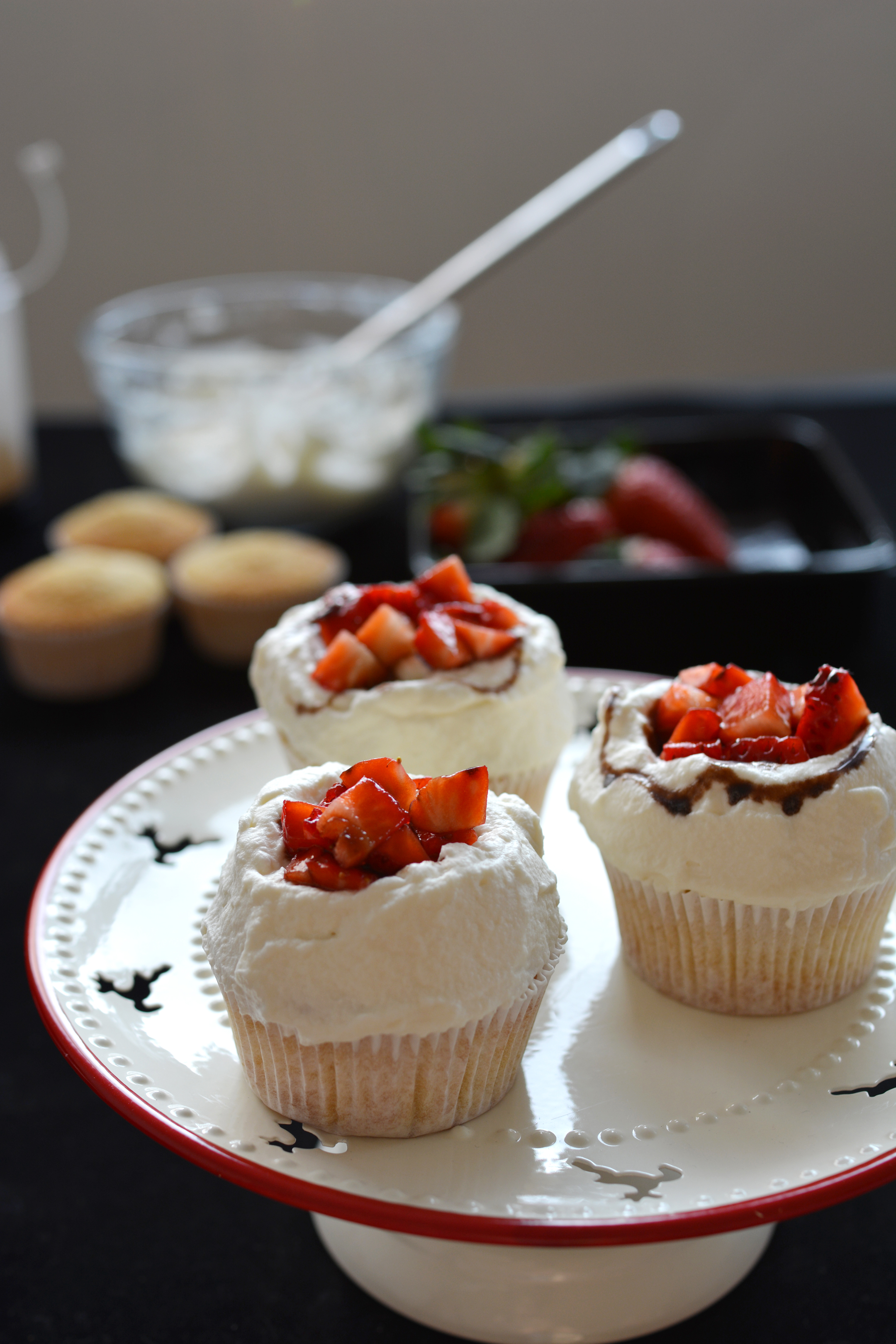 close-up view image of three cupcakes with fresh cream, strawberries, and balsamic vinegar glaze, beautifully presented on a cake table