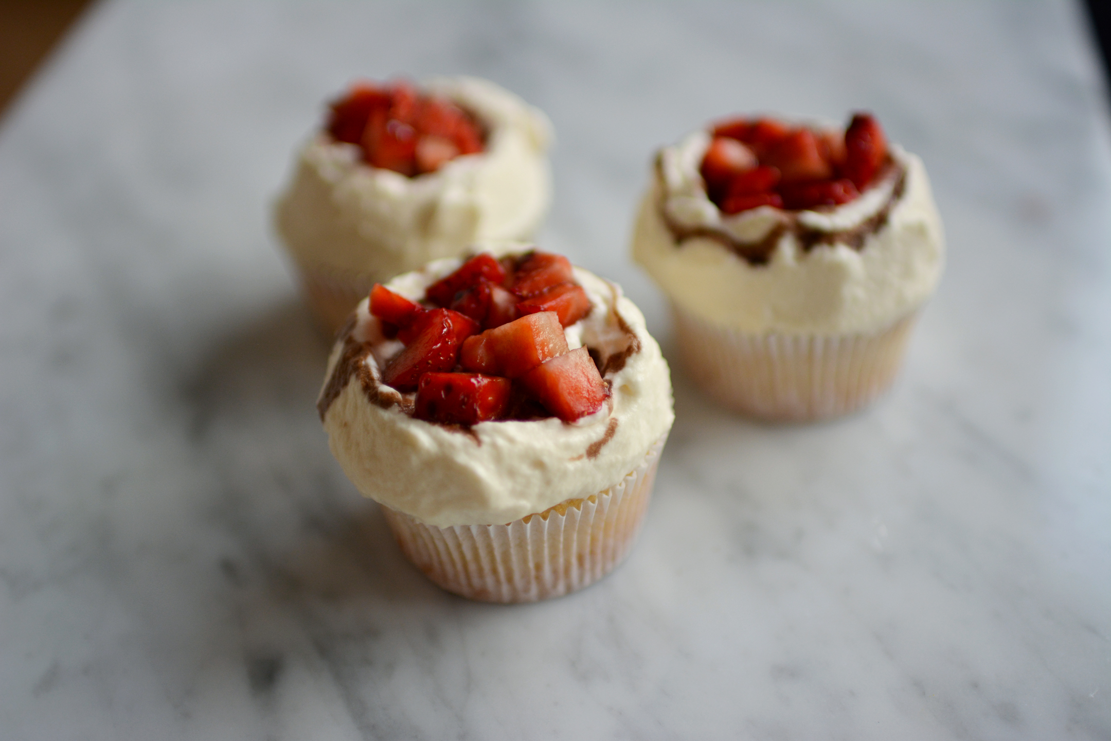 close-up view image of three cupcakes with fresh cream, strawberries, and balsamic vinegar glaze