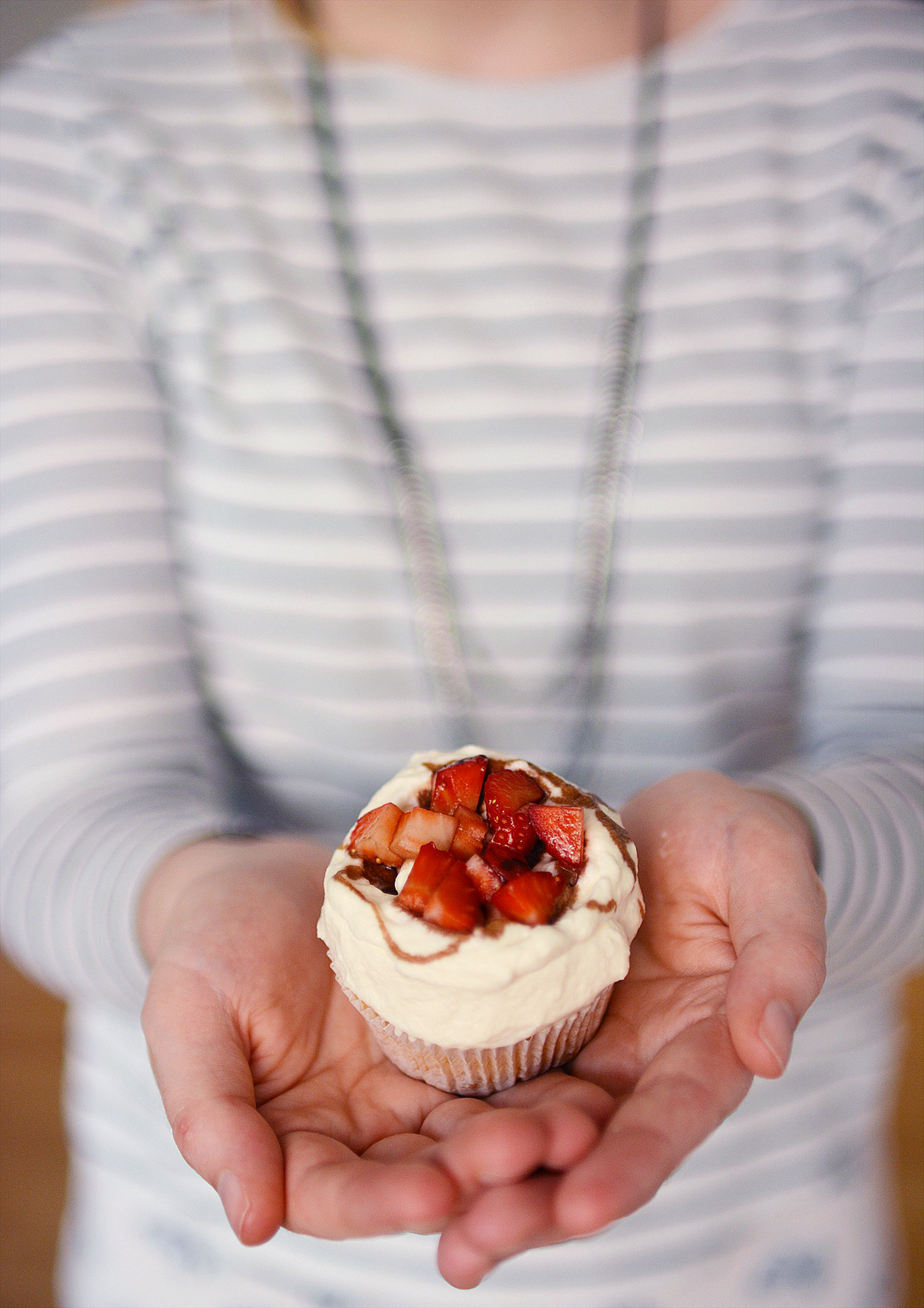 image of a woman holding a single cupcake with fresh cream, strawberries, and balsamic vinegar glaze in both hands
