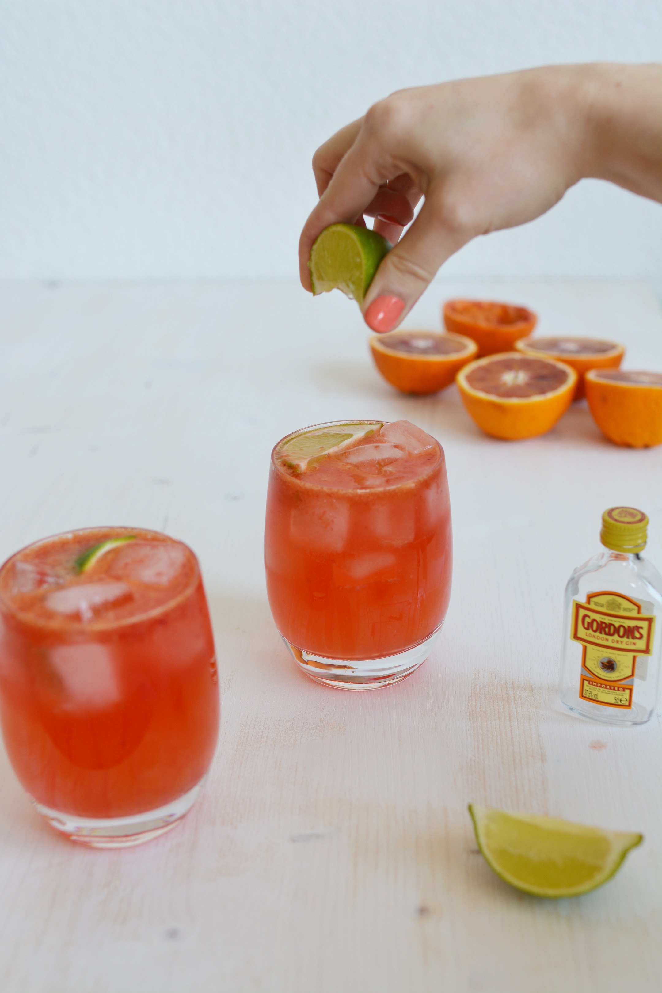 image of a hand squeezing a lime into one of two glasses of blood orange gin and tonic