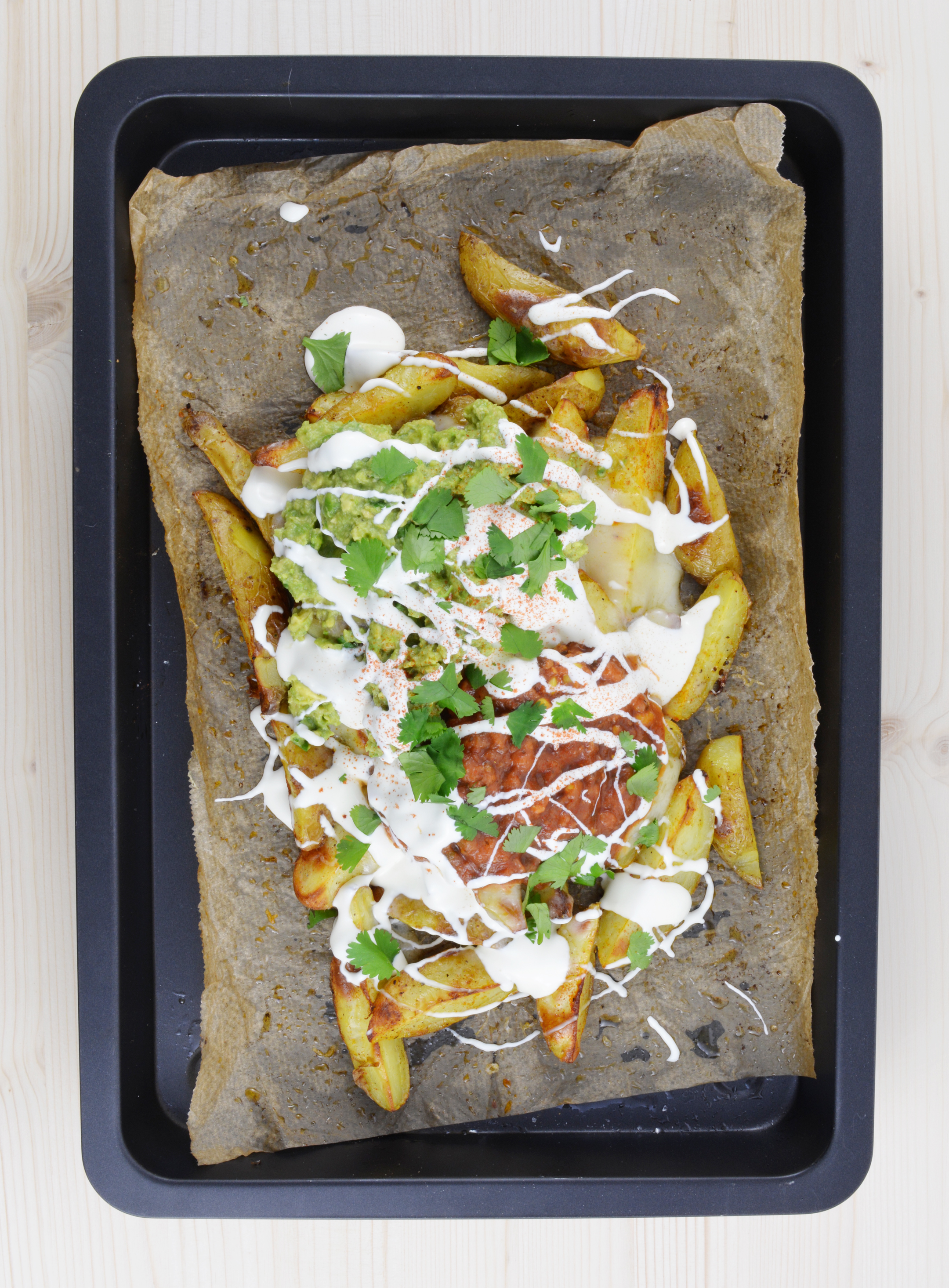 top down image of a potato wedges nachos  topped with guacamole, salsa and sour cream