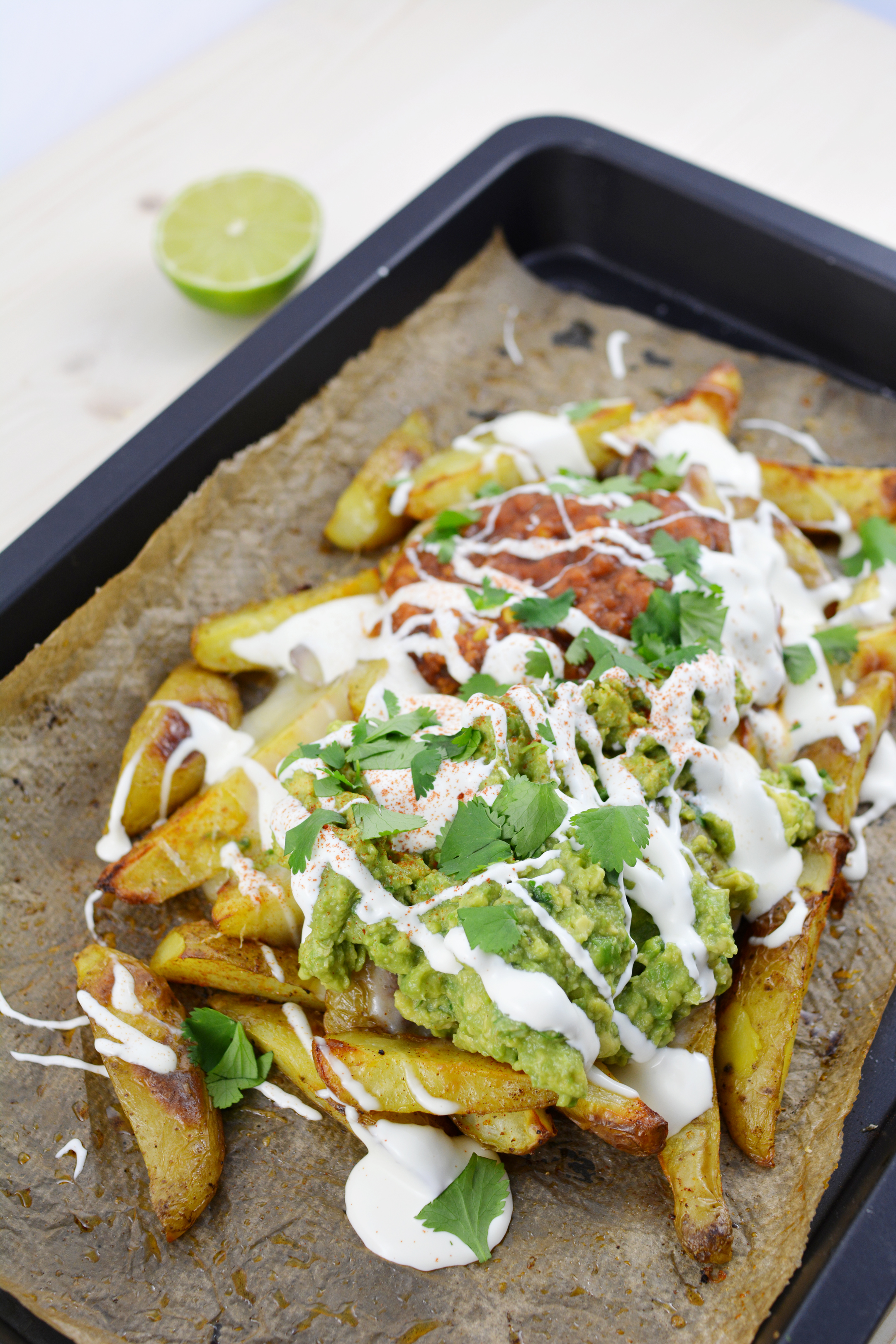 top down image of a potato wedges nachos topped with guacamole, salsa and sour cream