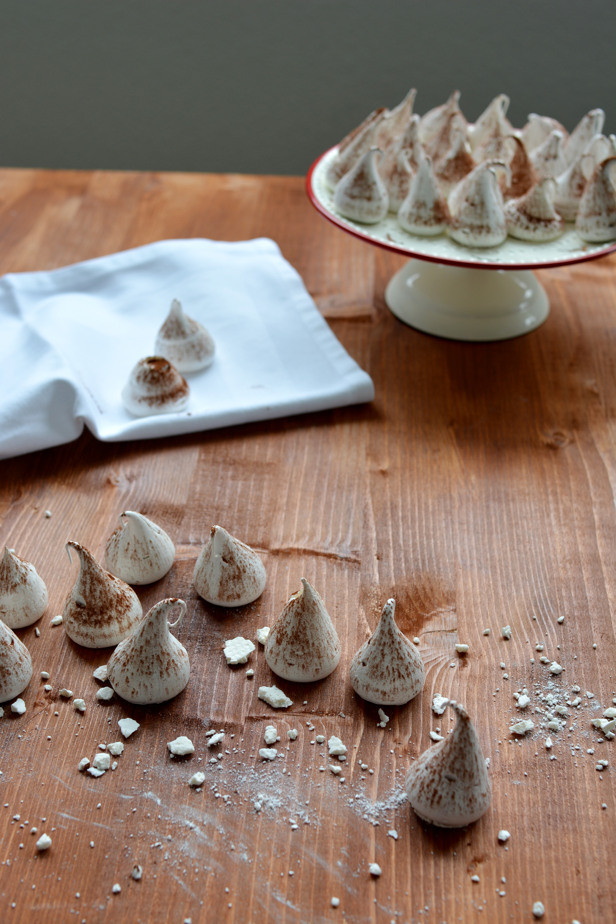 image of swiss meringue kisses, some arranged on a cake table and others scattered on the table
