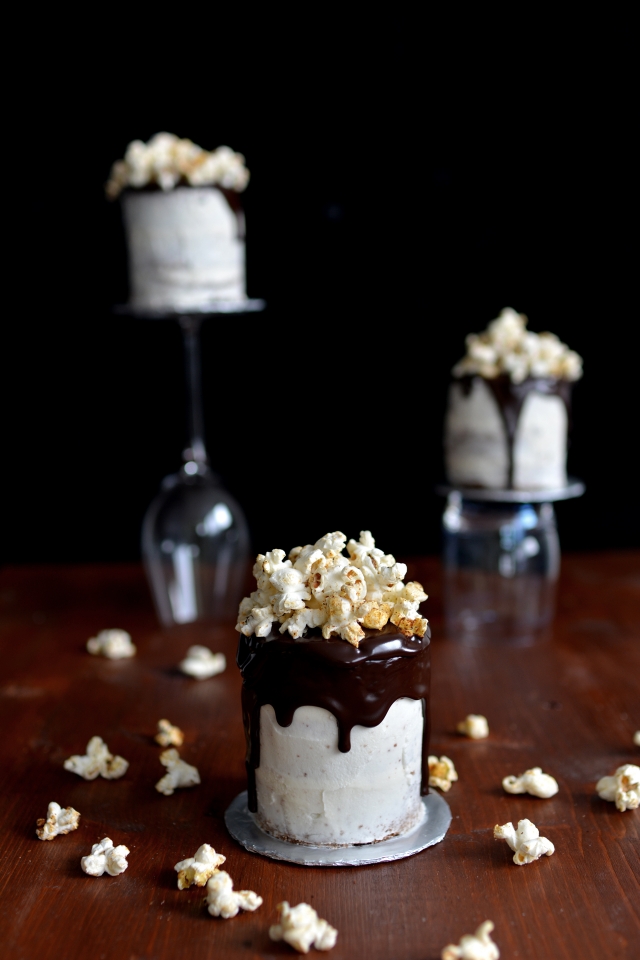 close-up image of a chocolate cake with chocolate syrup drizzle, topped with chili popcorn, and two additional cakes arranged on top of a champagne glass
