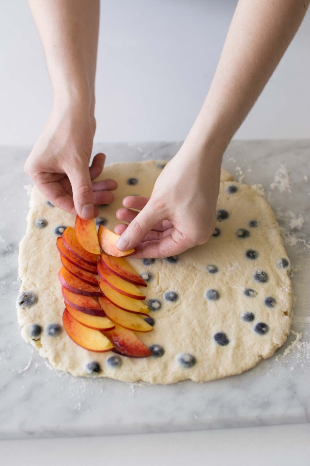 Placing nectarines onto rolled out Blueberry and Nectarine Scones  on a floured surface on a marble table.