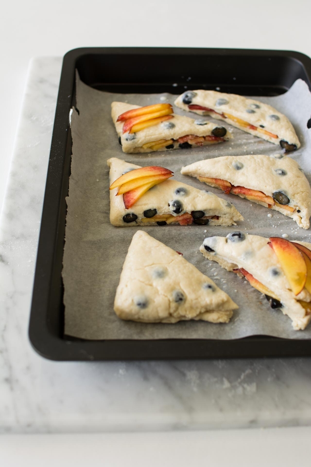 Blueberry and Nectarine Scones on parchment paper in a baking pan sitting on a marble table.