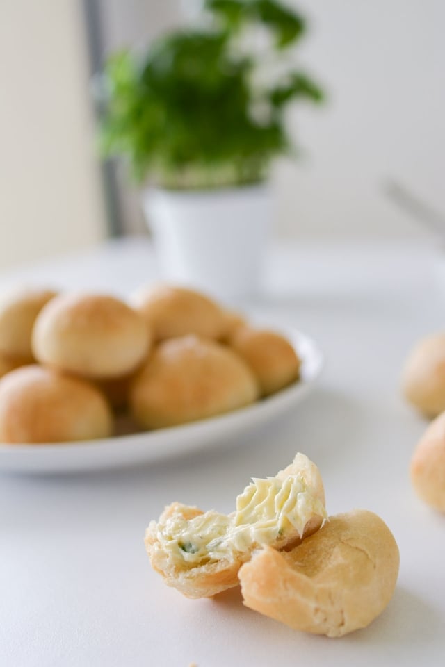 close-up image of a single doughball featuring a flavorful homemade garlic butter, with a plate full of neatly arranged doughballs in the background
