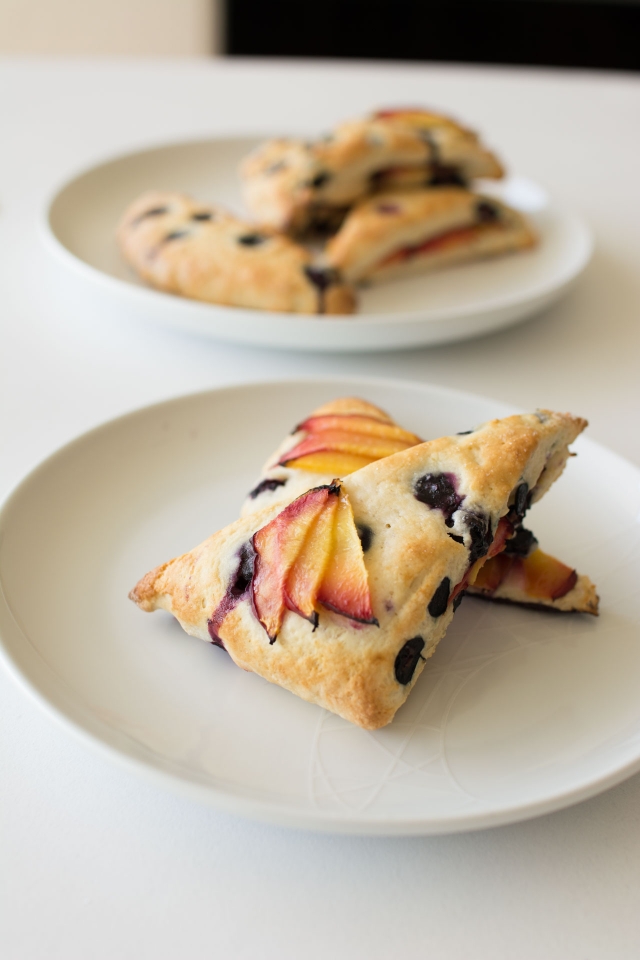 Baked Blueberry and Nectarine Scones on a white plate with more scones in the background on a white table.