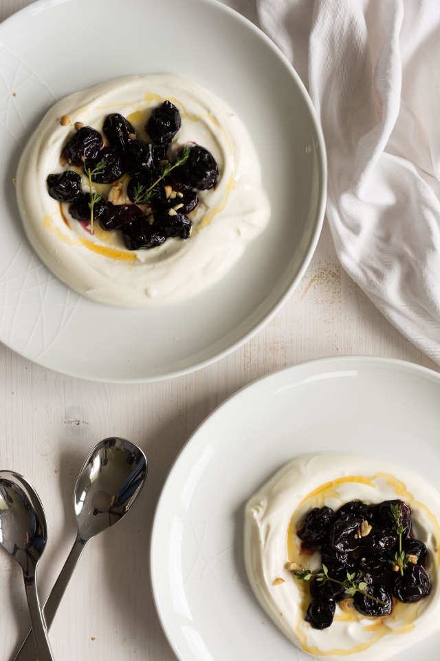 two round plates containing with yogurt topped with roasted grapes, and thyme, drizzled with honey.