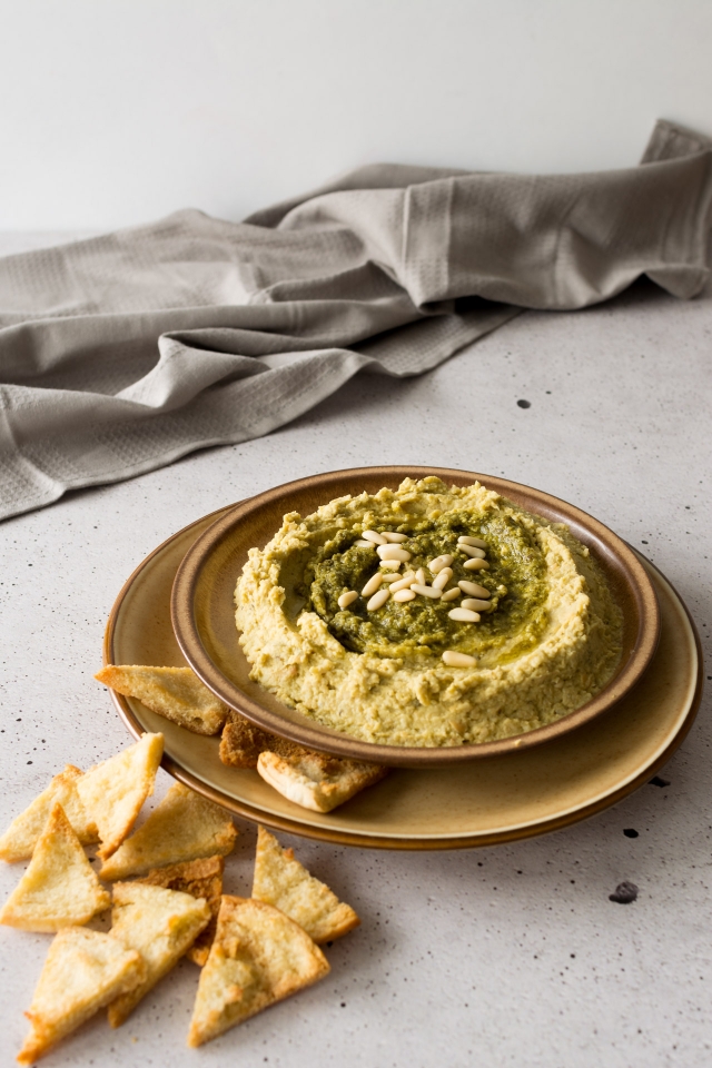 front view image of basil pesto hummus in a round plate with pita chips