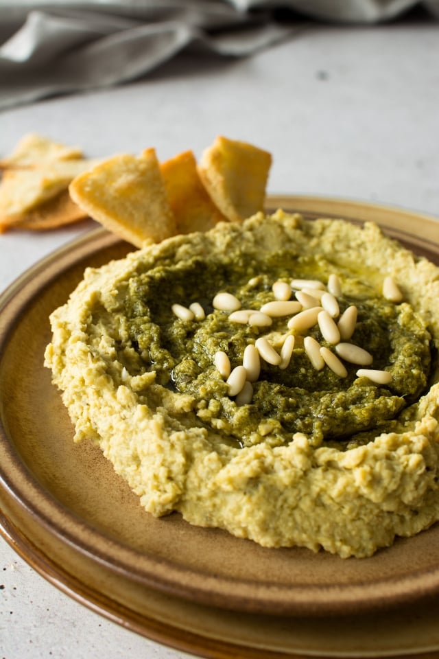 close up view of basil pesto hummus in a round plate with pita chips