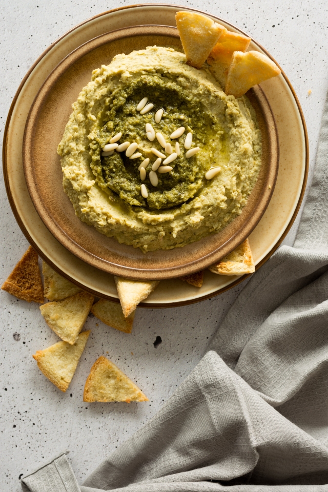 top view image of basil pesto hummus in a round plate with pita chips