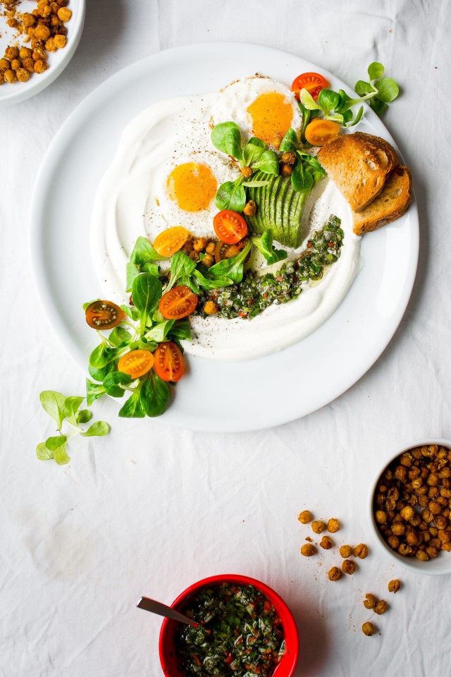 top down image of savory yogurt chimichurri salad, topped with spicy roasted chickpeas, slice avocado, tomatoes and eggs on the side
