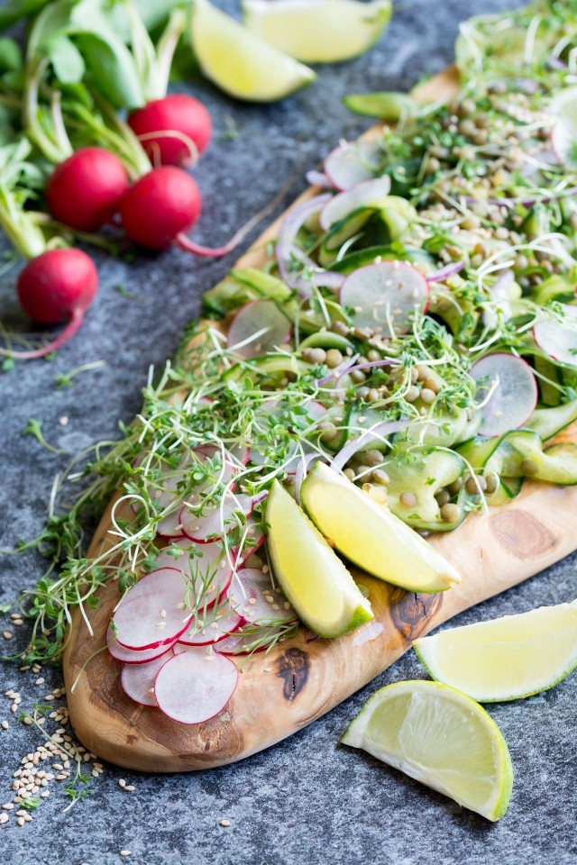 Side view of a cucumber and lentil salad with radishes on a wooden board and a bunch of radishes on the side. 
