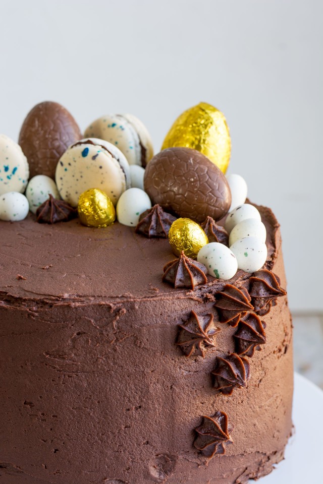 close up half image of a moist vanilla layer cake covered in chocolate orange frosting topped with chocolate eggs and macarons
