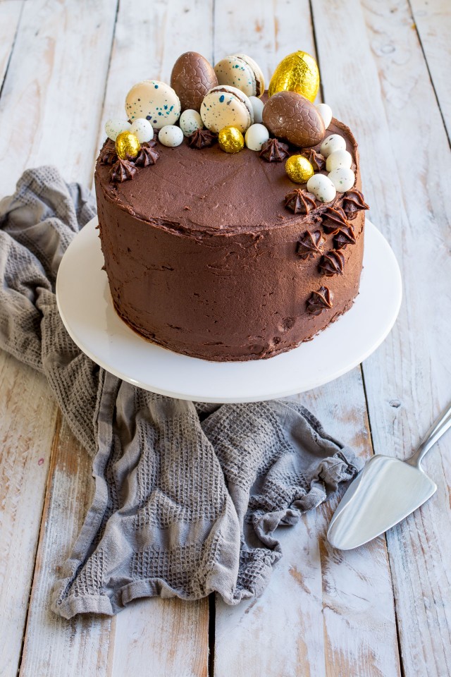 close up image of a moist vanilla layer cake covered in chocolate orange frosting topped with chocolate eggs and macarons
