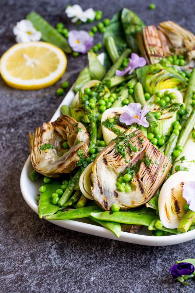 half photo of a serving dish containing grilled spring vegetables including french green beans, spring onions, sugar snap peas, asparagus, leeks, and artichokes, glisten with a homemade lemon parsley butter